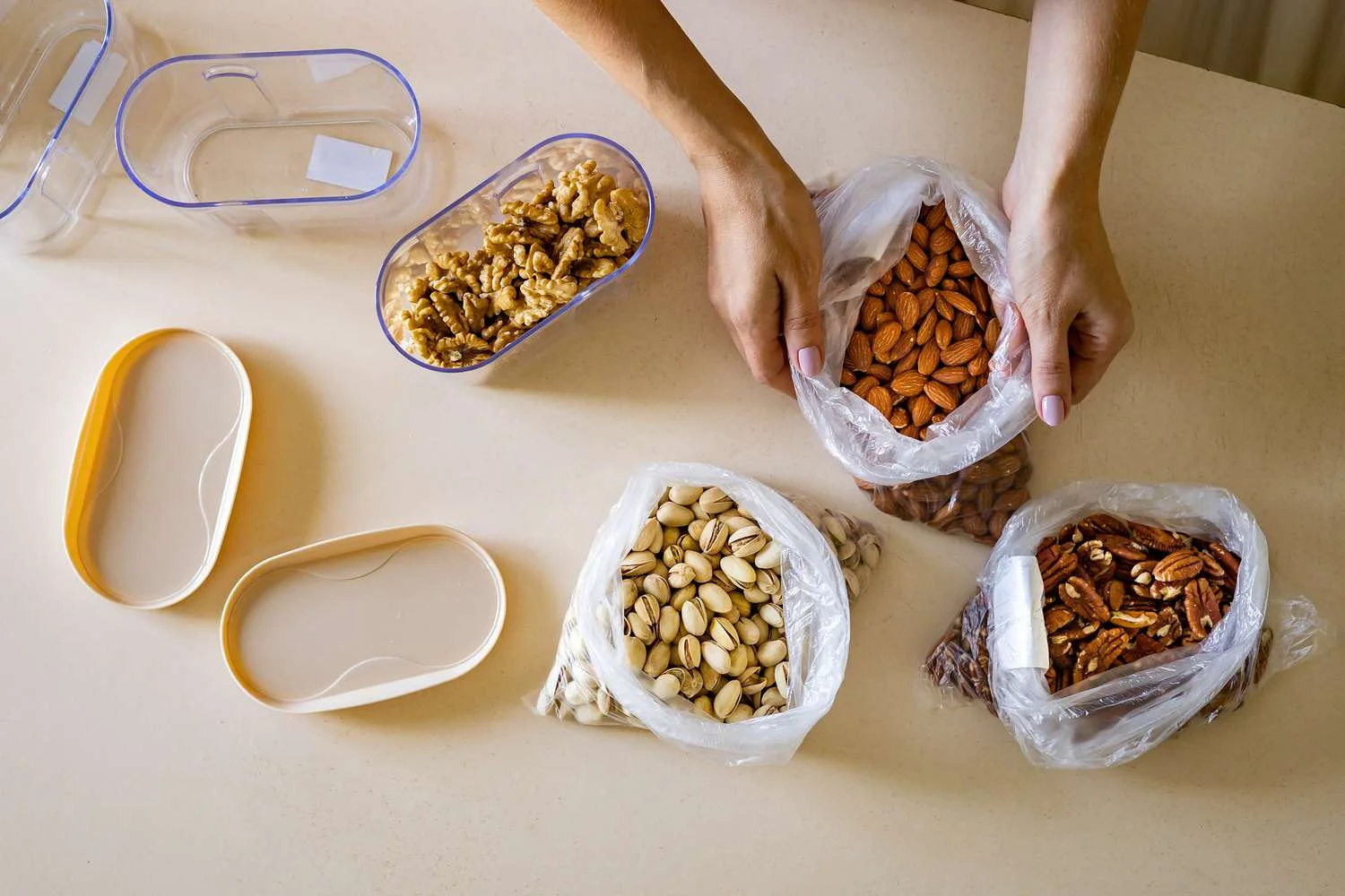 Organizing assorted nuts into plastic containers and bags on a light-colored kitchen countertop